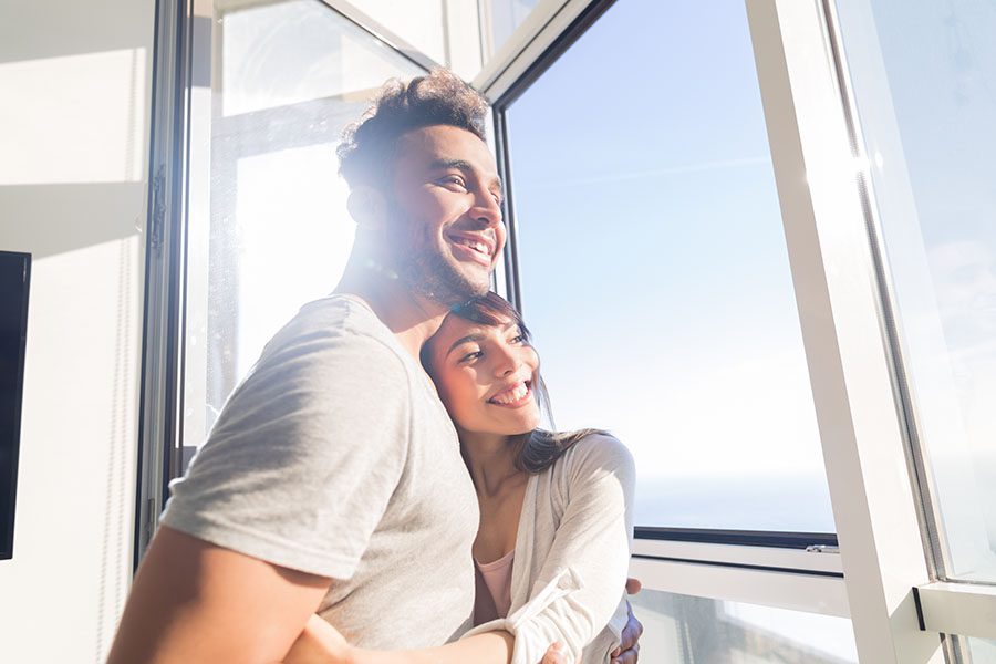 Personal Insurance - Happy Young Couple Looking Out the Window in Their Home