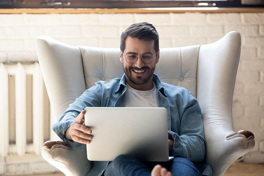 MassMutual FAQs - Portrait of a Smiling Man Sitting on a Lounge Chair Using His Laptop